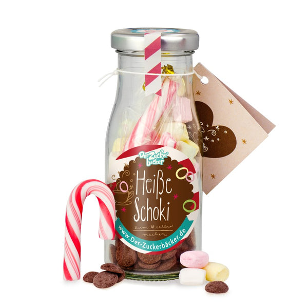 Milchflasche mit der Aufschrift "Heiße Schoki" und Süßigkeiten wie Marshmallows, Schokoplätzchen und Zuckerstange.