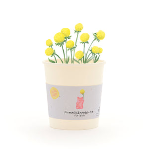 Becher mit gelben Gummibärchen-Blumen und einem Etikett, auf dem „Gummibärenblume für dich“ steht.