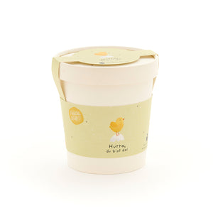 Becher mit gelbem Etikett, darauf ein Küken und die Aufschrift "Hurra, du bist da!"