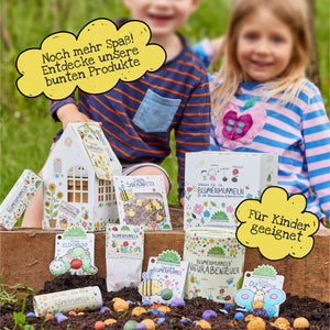 Zwei Kinder sitzen im Garten hinter einer Auswahl bunter Blumenprodukte mit spielerischen Verpackungen; gelbe Sprechblasen mit Text „Noch mehr Spaß! Entdecke unsere bunten Produkte“ und „Für Kinder geeignet“ ergänzen das Bild.