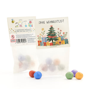 Geschenkverpackung mit Weihnachtsmotiv und bunten Saatkugeln in Blau, Lila, Grün, Gelb und Rot.