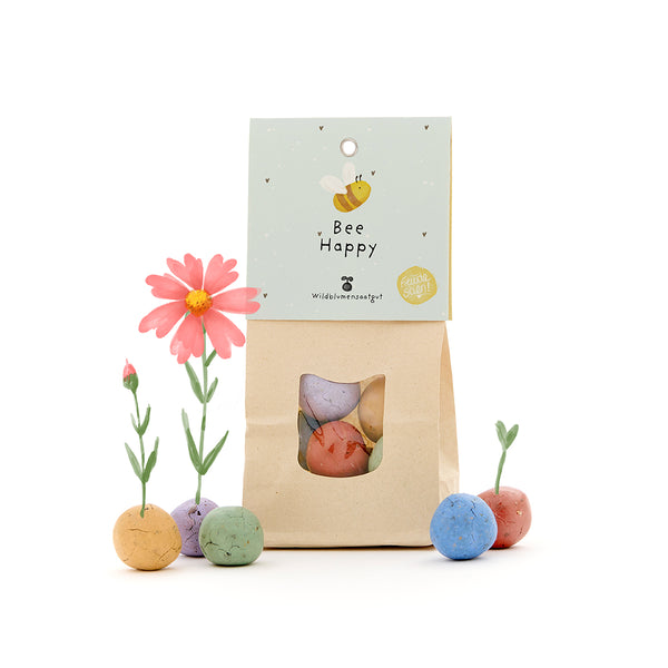 Papiertüte mit der Aufschrift "Bee Happy" und bunten Samenbomben, aus denen Blumen wachsen.