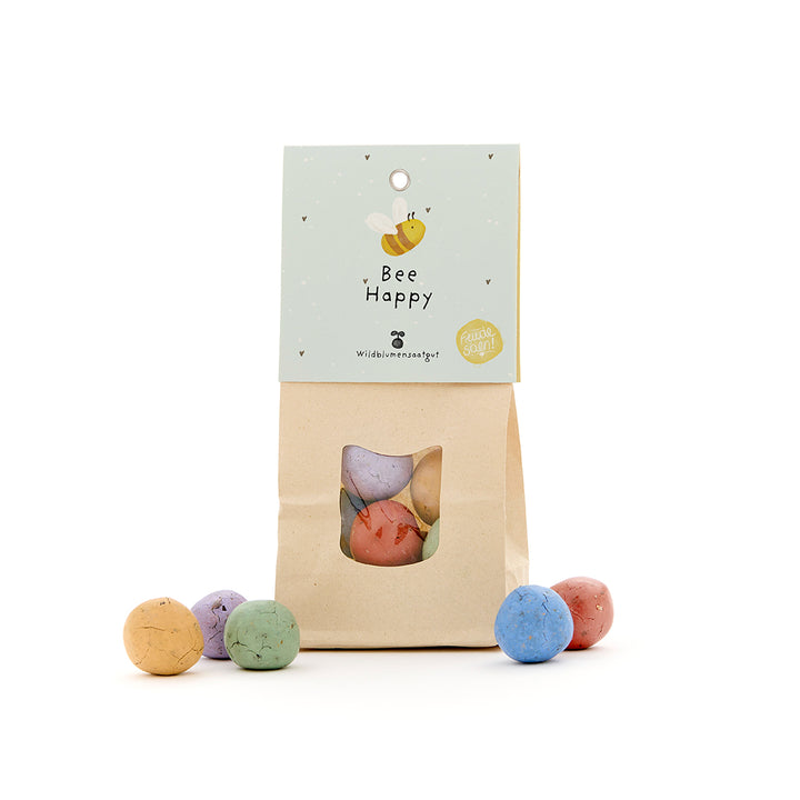 Papiertüte mit bunten Samenbomben und Etikett "Bee Happy" für Wildblumen.
