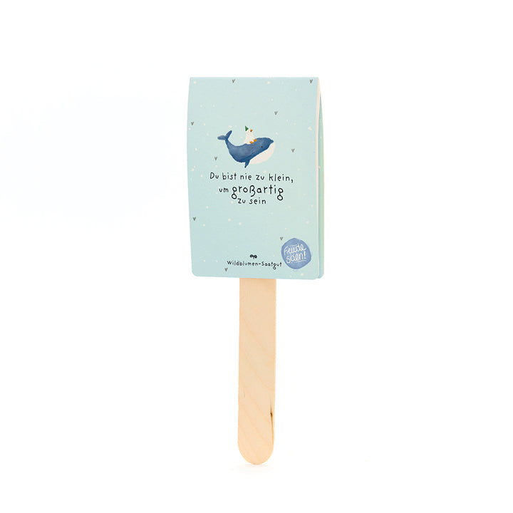 Holzstäbchen mit hellblauem Papieranhänger, darauf ein Wal mit Partyhut und der Text „Du bist nie zu klein, um großartig zu sein“.