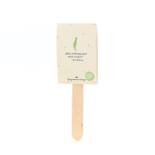 Ein Stiel mit einer Verpackung darauf, beschriftet mit „Das interessiert mich nicht. – die Bohne“, darunter ein gezeichneter grüne Bohne, für Stangenbohnen-Saatgut.