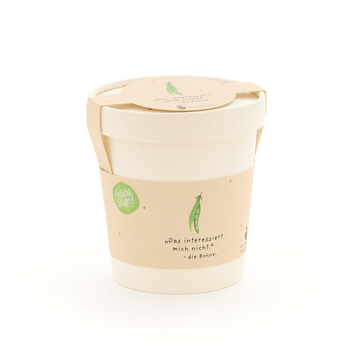 Ein weißer Becher mit beigem Etikett, auf dem eine grüne Erbse und der Spruch „Das interessiert mich nicht. – die Bohne“ abgebildet sind.
