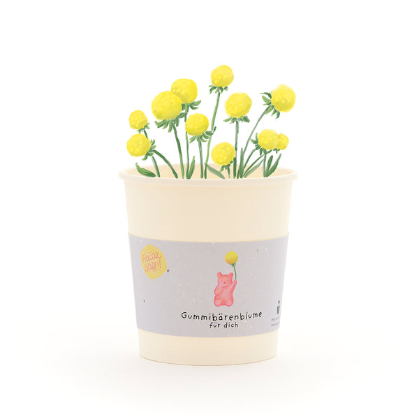 Becher mit gelben Gummibärchen-Blumen und einem Etikett, auf dem „Gummibärenblume für dich“ steht.