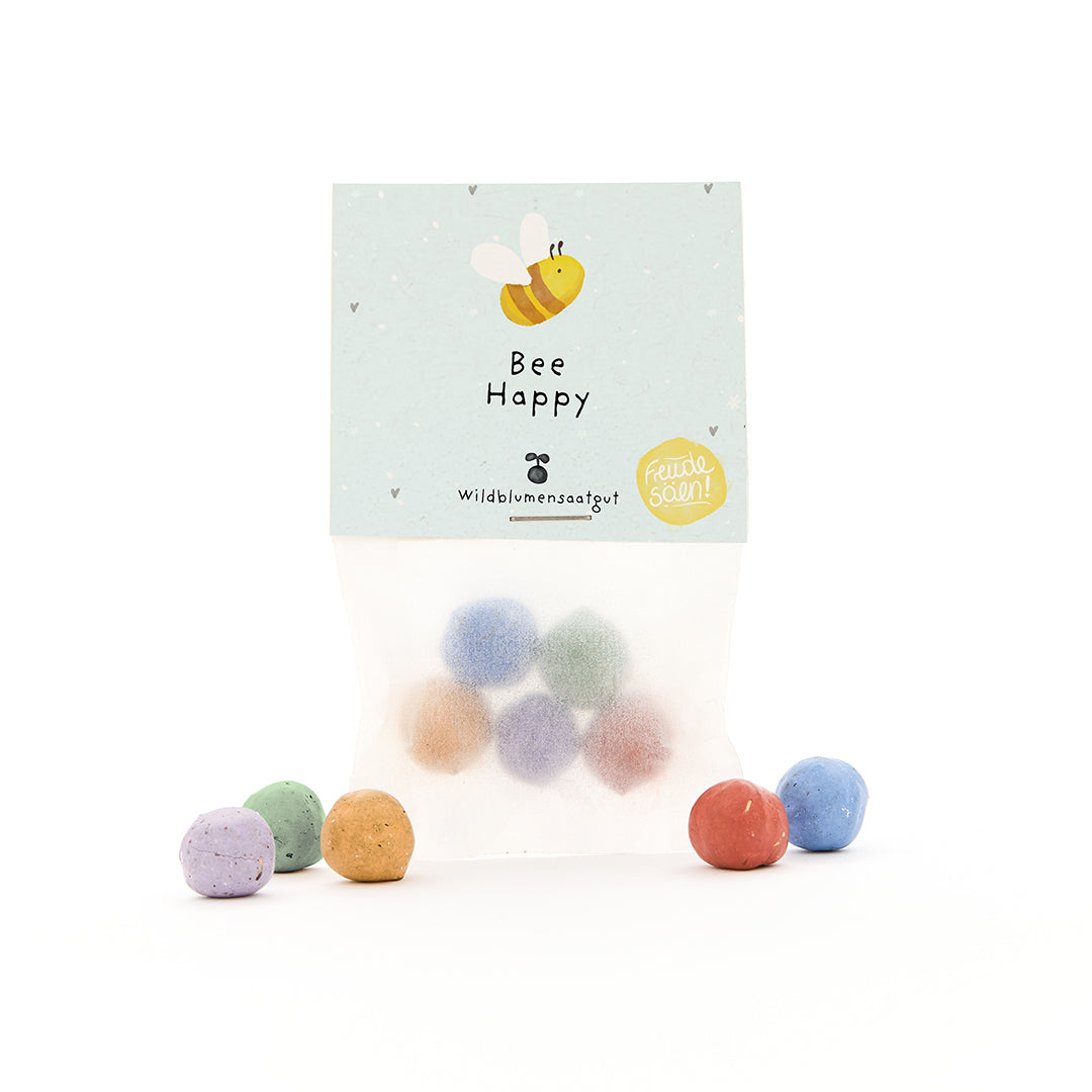 Tüte mit bunten Samenbomben und Etikett "Bee Happy" sowie einer gezeichneten Biene.