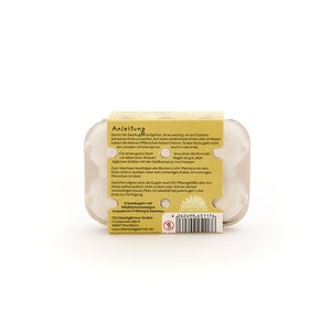 Rückseite einer kleinen Eierkartonverpackung mit aufgeklebter Anleitung zur Aussaat von Samen, Barcode und Herstellerinformationen auf Deutsch.