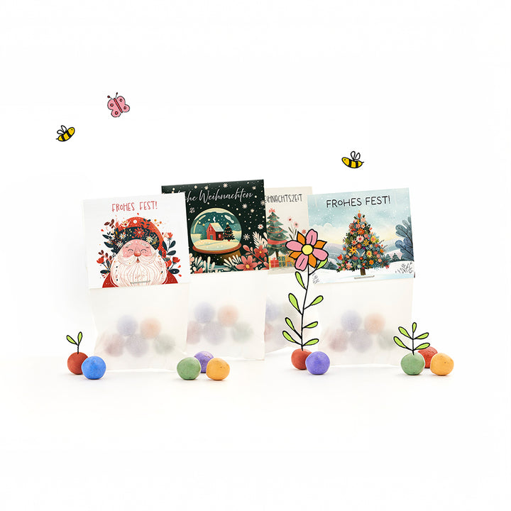 Drei weihnachtlich gestaltete Geschenktüten mit bunten Kugeln, illustrierten Weihnachtsmotiven und den Schriftzügen „Frohes Fest!“ sowie gezeichneten Blumen, Bienen und einem Schmetterling.