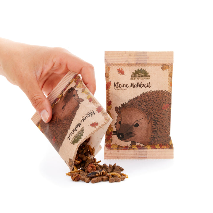 Hand kippt eine Packung mit Igel-Futter, daneben steht eine weitere ungeöffnete Packung mit einem gezeichneten Igel darauf.