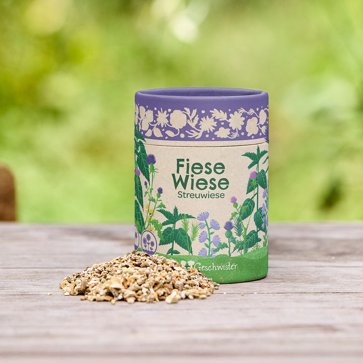 Dose mit der Aufschrift "Fiese Wiese Streuwiese" und einer Mischung von Samen auf einem Holztisch im Freien.