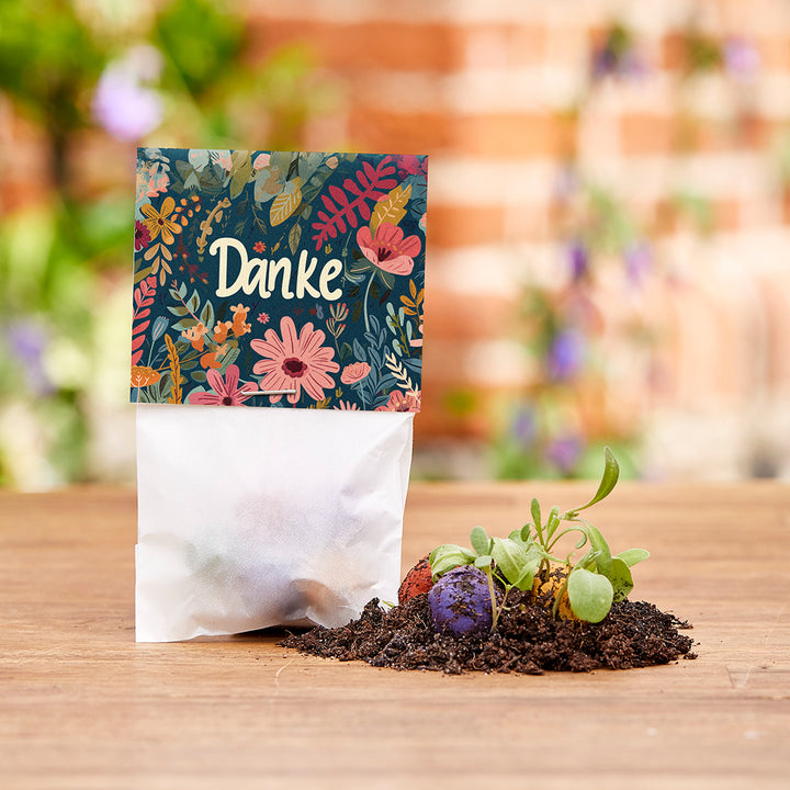Pflanzenset mit bunter Karte "Danke", Erdreich und kleinen Setzlingen auf Holztisch.