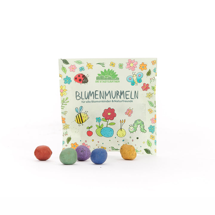 Paket mit der Aufschrift "Blumenmurmeln" und bunten, runden Kugeln davor; die Verpackung ist mit bunten Blumen, Insekten und Tieren illustriert.