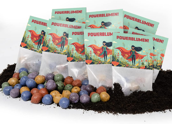 Mehrere Tütchen mit der Aufschrift "POWERBLUMEN!" und einer Superheldin-Illustration stehen in Erde, davor liegen bunte Samenbomben.