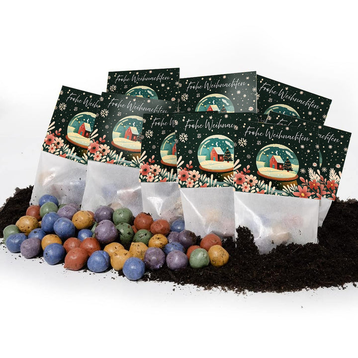 Mehrere Tütchen mit der Aufschrift "Frohe Weihnachten" und bunten Samenbällchen liegen auf Erde.