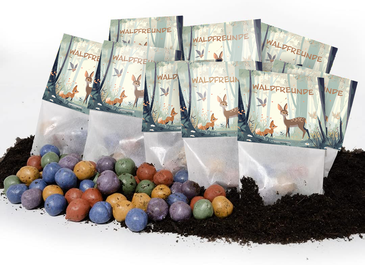 Mehrere Tütchen mit der Aufschrift "WALDFREUNDE" und Waldtier-Illustrationen stehen hinter bunten Samenbällchen auf Erde.