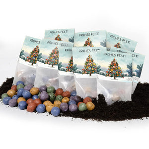 Mehrere Tütchen mit der Aufschrift "Frohes Fest!" und einem weihnachtlich geschmückten Baum, davor liegen bunte Samenbälle auf Erde.