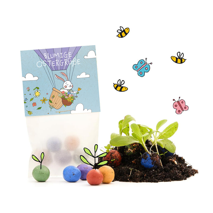 Tüte mit der Aufschrift „Blumige Ostergrüße“, daneben bunte Samenbomben, junge Pflanzen, Erde sowie gezeichnete Bienen und Schmetterlinge.