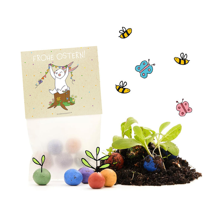 Ostergeschenk mit bunter Samenmischung, einer „Frohe Ostern“-Karte mit Hase, Samenbällchen und jungen Pflanzen, umgeben von gezeichneten Bienen und Schmetterlingen.