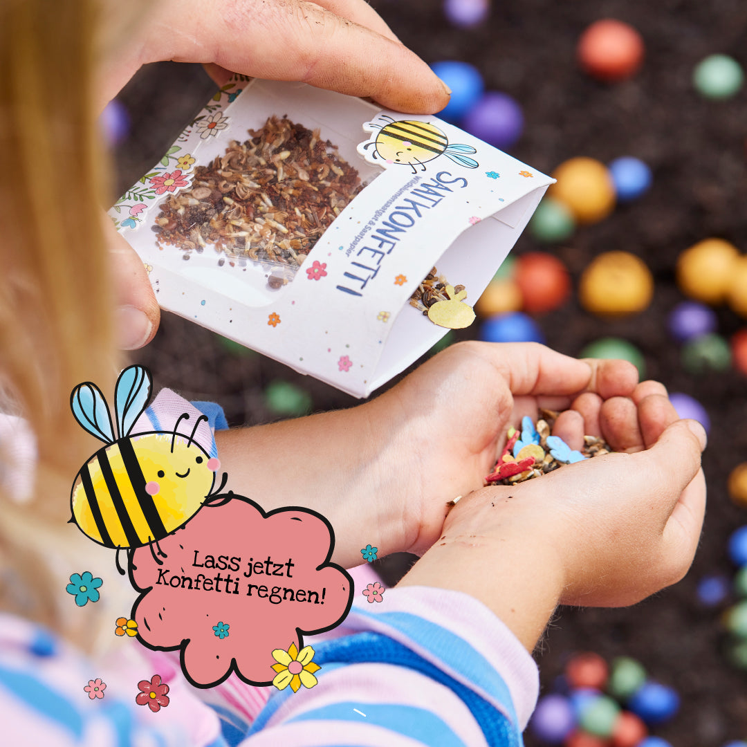 Ein Kind hält Samen-Konfetti in den Händen, während eine Packung mit Blumenmotiven darüber ausgeschüttet wird. Im Vordergrund eine gezeichnete Biene mit der Sprechblase "Lass jetzt Konfetti regnen!". Im Hintergrund bunte Kugeln auf Erde.