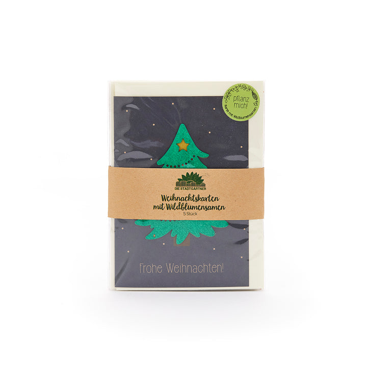 Weihnachtskarte mit grünem Weihnachtsbaum und Stern, in einer Verpackung mit braunem Papierband und der Aufschrift "Weihnachtskarten mit Wildblumensamen", daneben ein grüner Sticker mit "Pflanz mich".