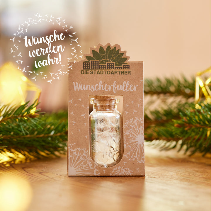 Ein kleines Glasfläschchen mit Korken auf einer Verpackung mit der Aufschrift "Die Stadtgärtner Wunscherfüller" neben Tannenzweigen und Weihnachtsdekoration.