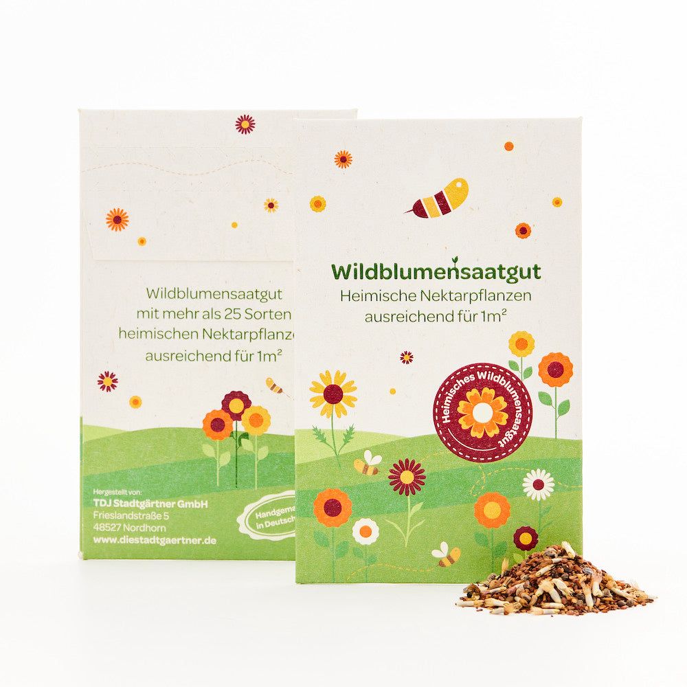 Zwei Packungen Wildblumensaatgut mit buntem Blumen- und Bienenmotiv sowie ein kleiner Haufen Saatgut davor.