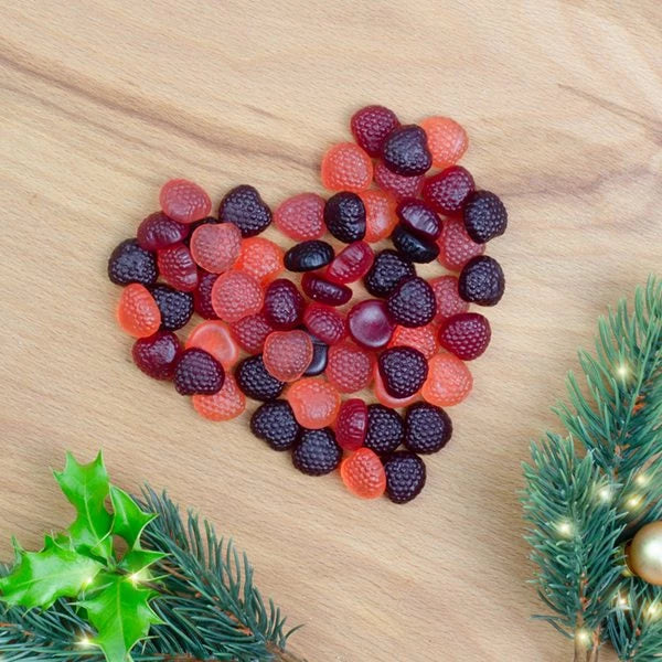 Gummibärchen in Herzform auf Holzuntergrund mit Tannenzweig und Stechpalmenblatt"