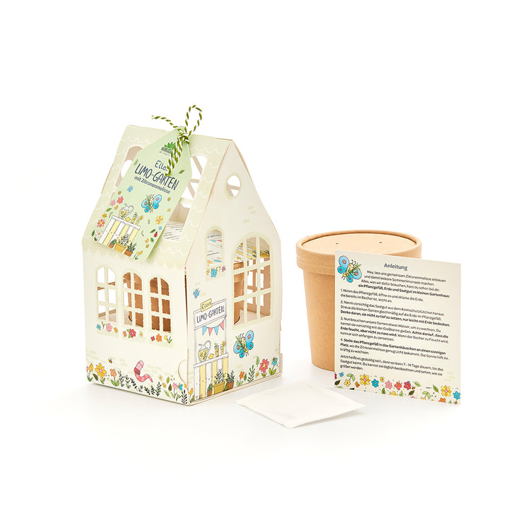 Ein Bastelset für Kinder zum Anpflanzen von Zitronenmelisse, bestehend aus einem dekorativen Papphaus, einem Blumentopf, einem Beutel mit Samen und einer Anleitung.