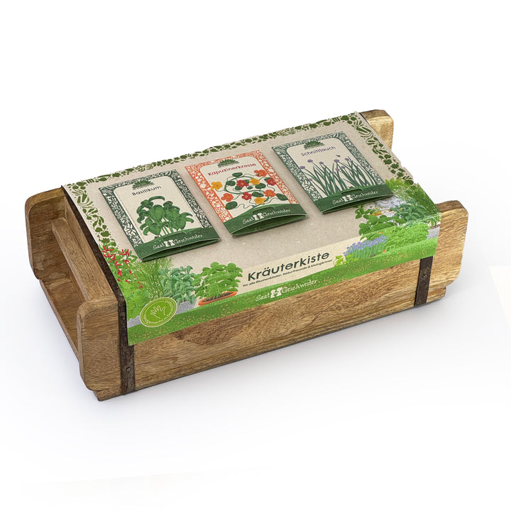 Holzkiste mit drei Samentüten für Kräuter (Basilikum, Kapuzinerkresse, Schnittlauch) und Aufschrift "Kräuterkiste" auf einer Banderole.