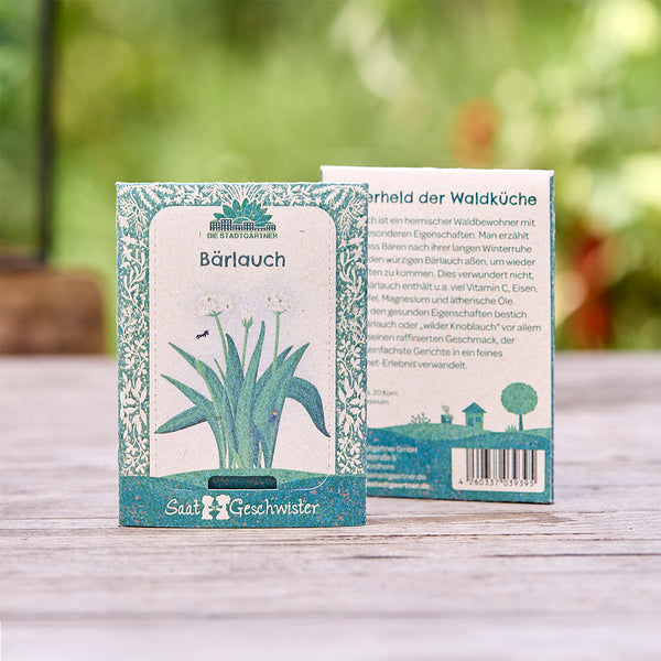 Zwei Samenpäckchen für Bärlauch von "Die Stadtgärtner" mit botanischer Illustration, auf einem Holztisch im Freien.