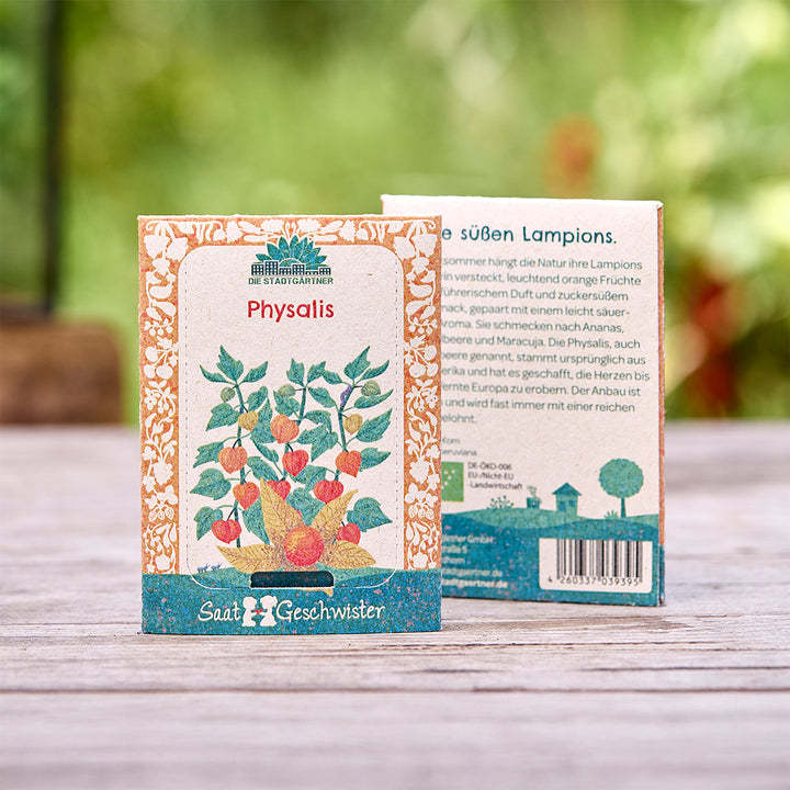 Zwei Saatgutverpackungen für Physalis der Marke "Die Stadtgärtner" stehen auf einem Holztisch, mit einer illustrierten Pflanze auf der Vorderseite und Text auf der Rückseite.