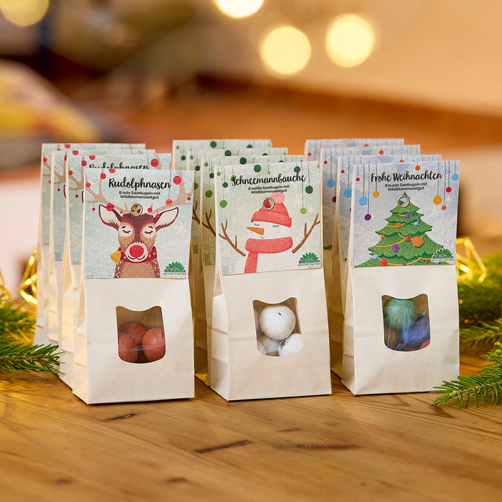 Drei weihnachtlich dekorierte Geschenktüten mit Süßigkeiten auf einem Holztisch, jeweils mit den Aufschriften "Rudolphnasen", "Schneemannbäuche" und "Frohe Weihnachten".