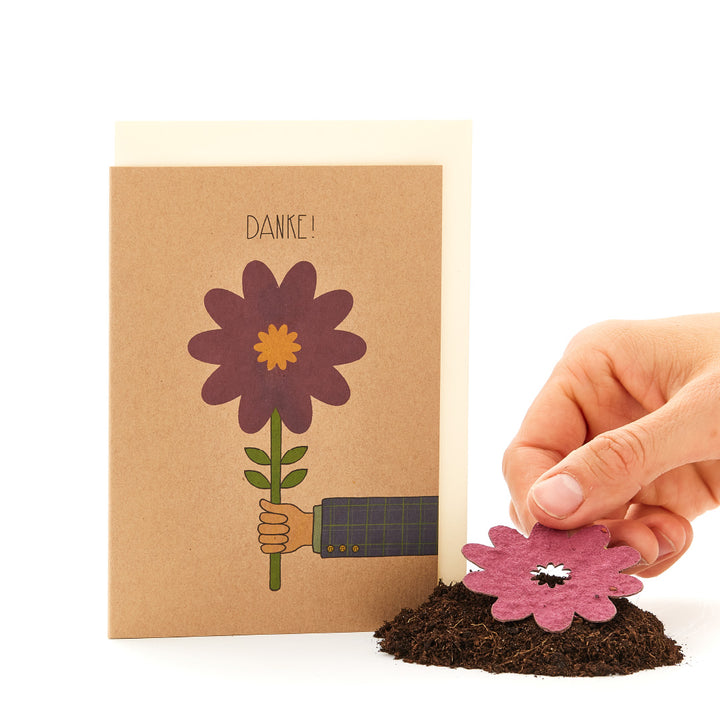 Hand hält eine Papierblume neben einer Dankeskarte mit gezeichneter Blume.