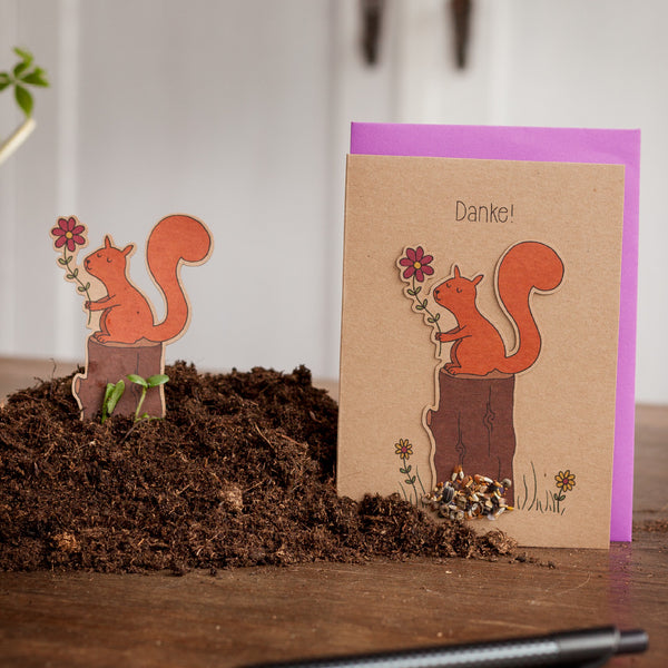 Grußkarte mit Eichhörnchen-Motiv und dem Wort "Danke!" darauf, neben einer ausgeschnittenen Eichhörnchen-Figur auf Erde.