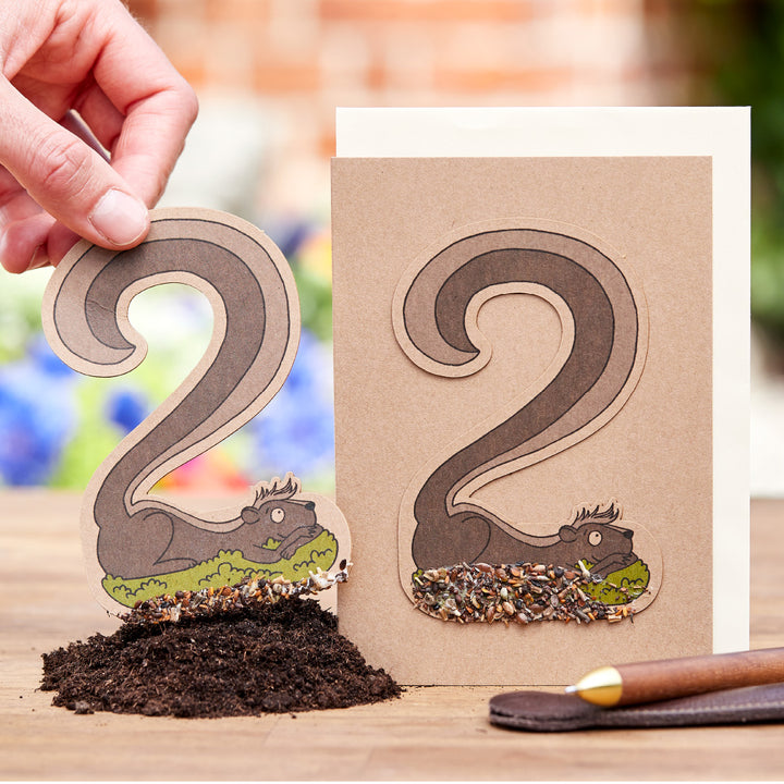 Hand hält eine Gartenkarte mit ausgestanzten Eichhörnchenmotiven, durch die Vogelsamen sichtbar sind.