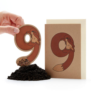 Hand hält einen ausgestanzten Buchstaben "ö" mit einem Fuchsdesign neben einer Karte mit dem gleichen Design und einem kleinen Erdhaufen.