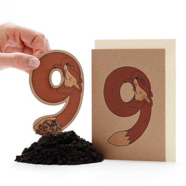 Hand hält einen ausgestanzten Buchstaben "ö" mit einem Fuchsdesign neben einer Karte mit dem gleichen Design und einem kleinen Erdhaufen.