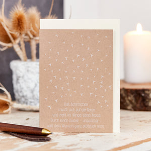 Grußkarte mit Schirmchen-Motiv und deutschem Spruch, auf Holztisch neben Trockenblumen und Kerze.
