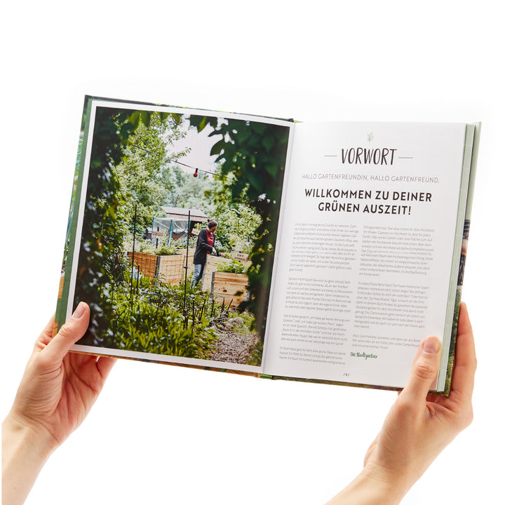 Person hält ein aufgeschlagenes Buch mit dem Titel "Vorwort" und einem Bild von einem Garten.